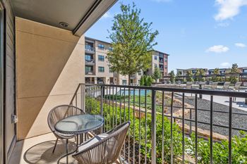 A balcony with a chair and table overlooking a pool and buildings. at Aurora Watson Branch, Texas